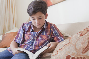 Hispanic boy reading book on sofa - BLEF04636