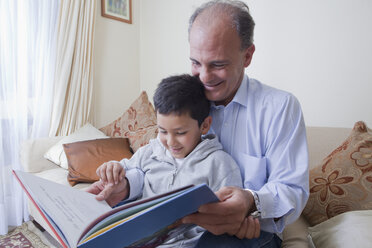 Hispanic father and son reading book on sofa - BLEF04640