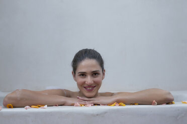 Lächelnde kaukasische Frau in der Badewanne mit Blumenblättern - BLEF04676