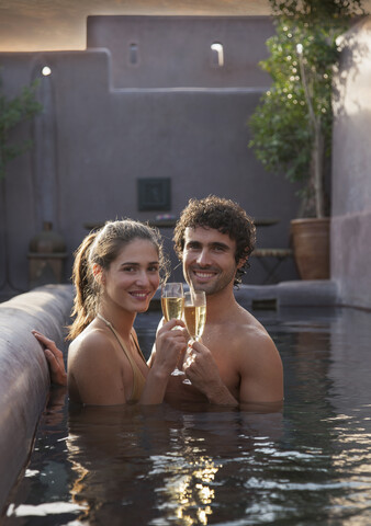 Lächelndes kaukasisches Paar, das mit Champagner im Schwimmbad anstößt, lizenzfreies Stockfoto
