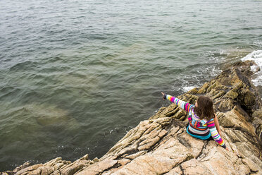 Kaukasisches Mädchen sitzt auf Felsen und zeigt auf den Ozean - BLEF04693
