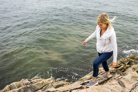 Kaukasische Frau, die auf Felsen am Meer läuft, lizenzfreies Stockfoto