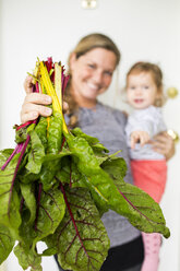 Lächelnde kaukasische Mutter hält Tochter und zeigt Salat - BLEF04697