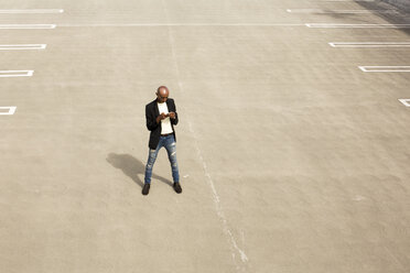 Gay Black man texting in empty parking lot - BLEF04705