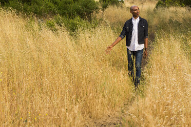 Pensive gay Black man walking in tall grass - BLEF04712
