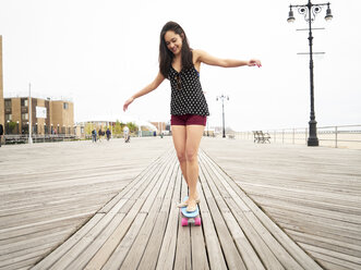 Gemischtrassige Frau fährt Skateboard auf der Strandpromenade - BLEF04788