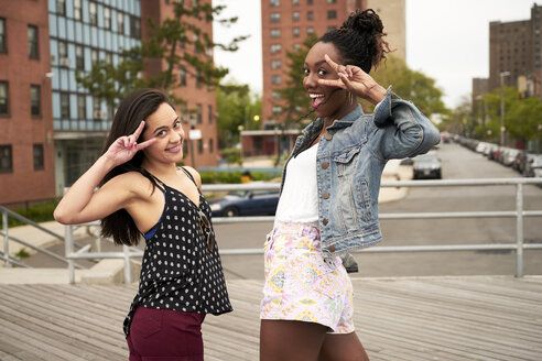 Smiling women gesturing peace on city boardwalk - BLEF04791