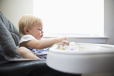 Caucasian baby girl self-feeding in high chair - BLEF04819