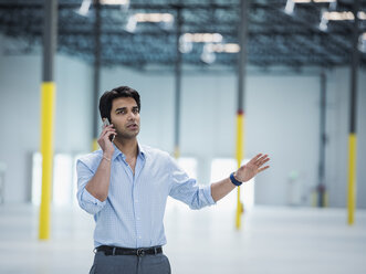 Indian businessman talking on cell phone in empty warehouse - BLEF04851