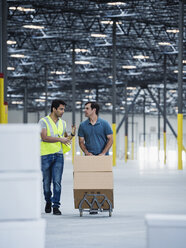 Workers pushing cardboard boxes on hand truck in warehouse - BLEF04882