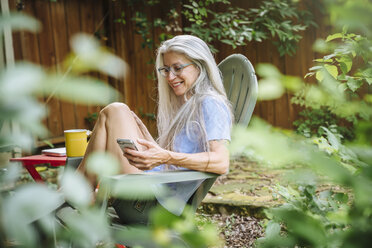 Kaukasische Frau, die im Garten mit ihrem Handy telefoniert - BLEF04903