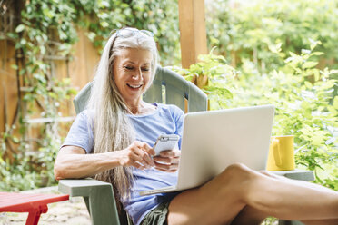 Kaukasische Frau mit Handy und Laptop auf der Terrasse im Hinterhof - BLEF04904