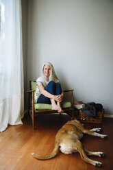 Kaukasische Frau sitzt in einem Sessel neben einem Hund - BLEF04916