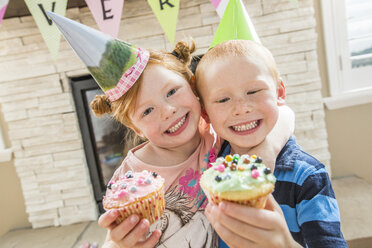 Kaukasischer Junge und Mädchen mit Partyhüten, die Cupcakes zeigen - BLEF04961