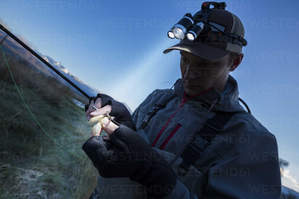 Caucasian man wearing headlamp baiting hook at dawn stock photo