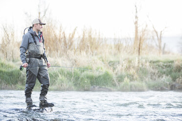 Caucasian man fly fishing on rock in river - BLEF04971