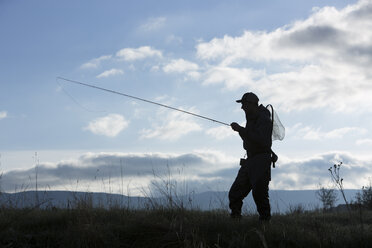 Silhouette of Caucasian man carrying fishing rod in field - BLEF04974