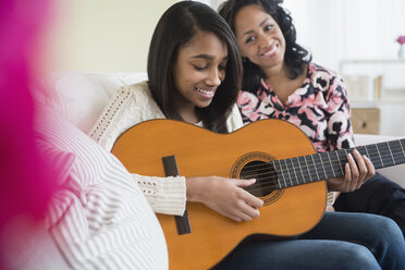 Mother watching daughter play guitar on sofa - BLEF05030