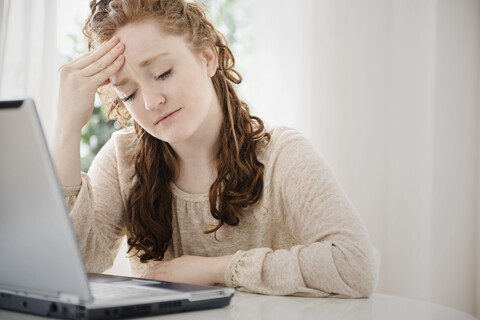 Kaukasische Frau mit Laptop reibt sich die Stirn, lizenzfreies Stockfoto