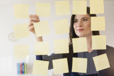 Caucasian businesswoman arranging adhesive notes on glass wall - BLEF05082