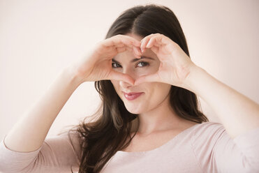 Caucasian woman gesturing heart-shape with hands over eyes - BLEF05085