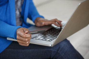 Schwarze Frau beim Online-Shopping mit Kreditkarte und Laptop auf dem Sofa - BLEF05112