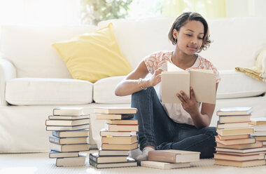 Black woman sitting on floor reading pile of books - BLEF05218