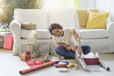 Black woman sitting on floor wrapping gifts - BLEF05220