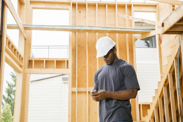 Schwarzer Bauarbeiter schreibt eine SMS mit seinem Handy - BLEF05301