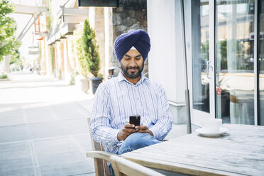 Mann mit Turban, der in einem Café eine SMS auf seinem Handy schreibt - BLEF05306