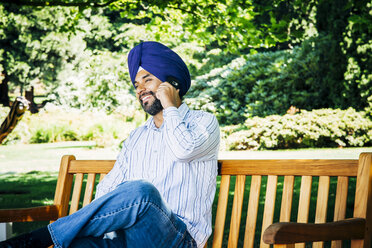 Man wearing turban sitting on park bench talking on cell phone - BLEF05311