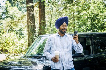 Man wearing turban posing for cell phone selfie at car - BLEF05312