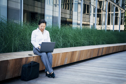 Geschäftsfrau sitzt auf einer Bank und benutzt einen Laptop - BLEF05314