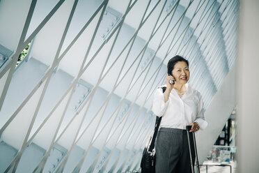 Businesswoman standing in lobby with suitcase talking on cell phone - BLEF05317