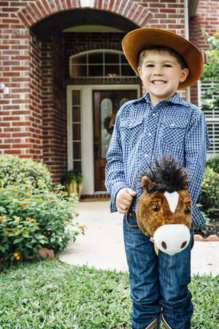 Weißer Junge im Cowboy-Kostüm reitet Spielzeugpferd, lizenzfreies Stockfoto