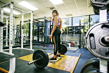 Mixed Race woman standing over barbell in gymnasium - BLEF05411