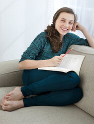 Smiling teenage girl doing homework on sofa - BLEF05436