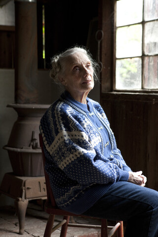 Ältere kaukasische Frau sitzt auf einem Stuhl, lizenzfreies Stockfoto