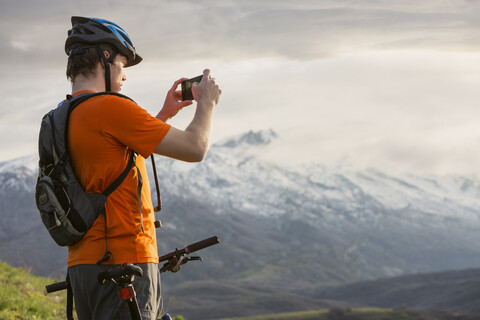 Kaukasischer Mann auf dem Mountainbike beim Fotografieren einer malerischen Aussicht, lizenzfreies Stockfoto