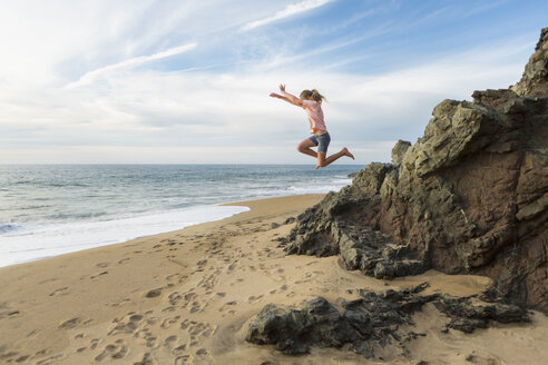 Kaukasisches Mädchen springt von Felsen am Strand - BLEF05542