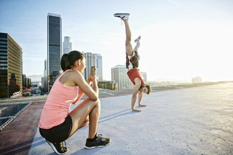 Woman photographing man doing handstand on urban rooftop stock photo