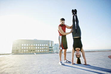 Caucasian man helping woman do handstand on urban rooftop - BLEF05556