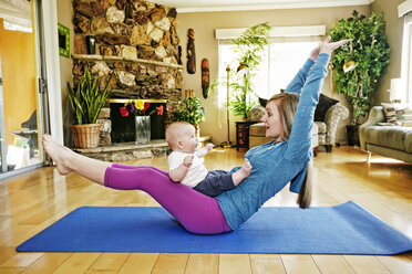 Mother working out on exercise mat with baby in lap - BLEF05558