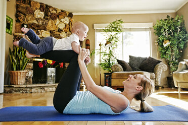 Mother working out on exercise mat balancing baby on legs - BLEF05560