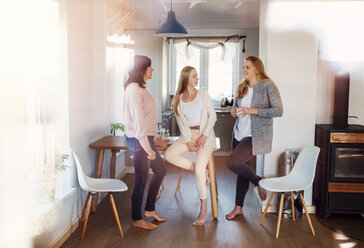 Mother and daughters standing in kitchen, talking, drinking coffee - HAPF02885