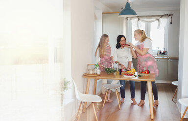 Mother and daughters standing in kitchen, preparing food, chopping vegetables - HAPF02899