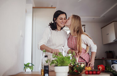 Tochter küsst Mutter, während sie in der Küche Gemüse schneidet - HAPF02908