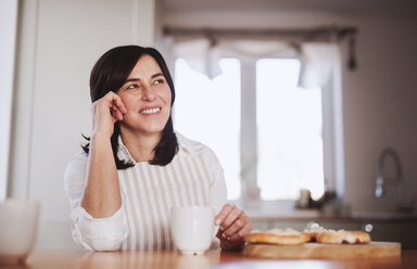 Mature woman sitting at kitchen table, drinking coffee - HAPF02917