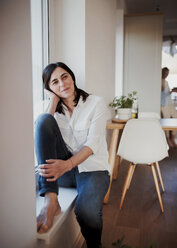 Mature woman sitting on windowsill in the kitchen, daydreaming - HAPF02931