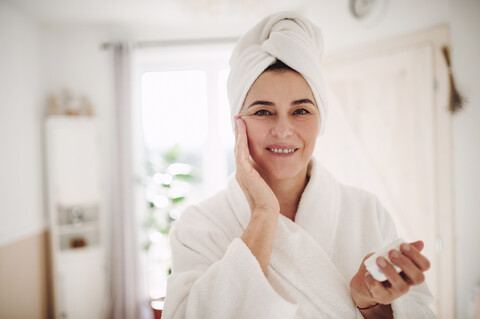 Porträt einer reifen Frau in einem Badezimmer zu Hause beim Auftragen von Feuchtigkeitscreme, lizenzfreies Stockfoto